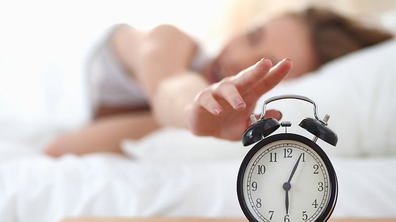 Young sleeping woman and alarm clock in bedroom at home